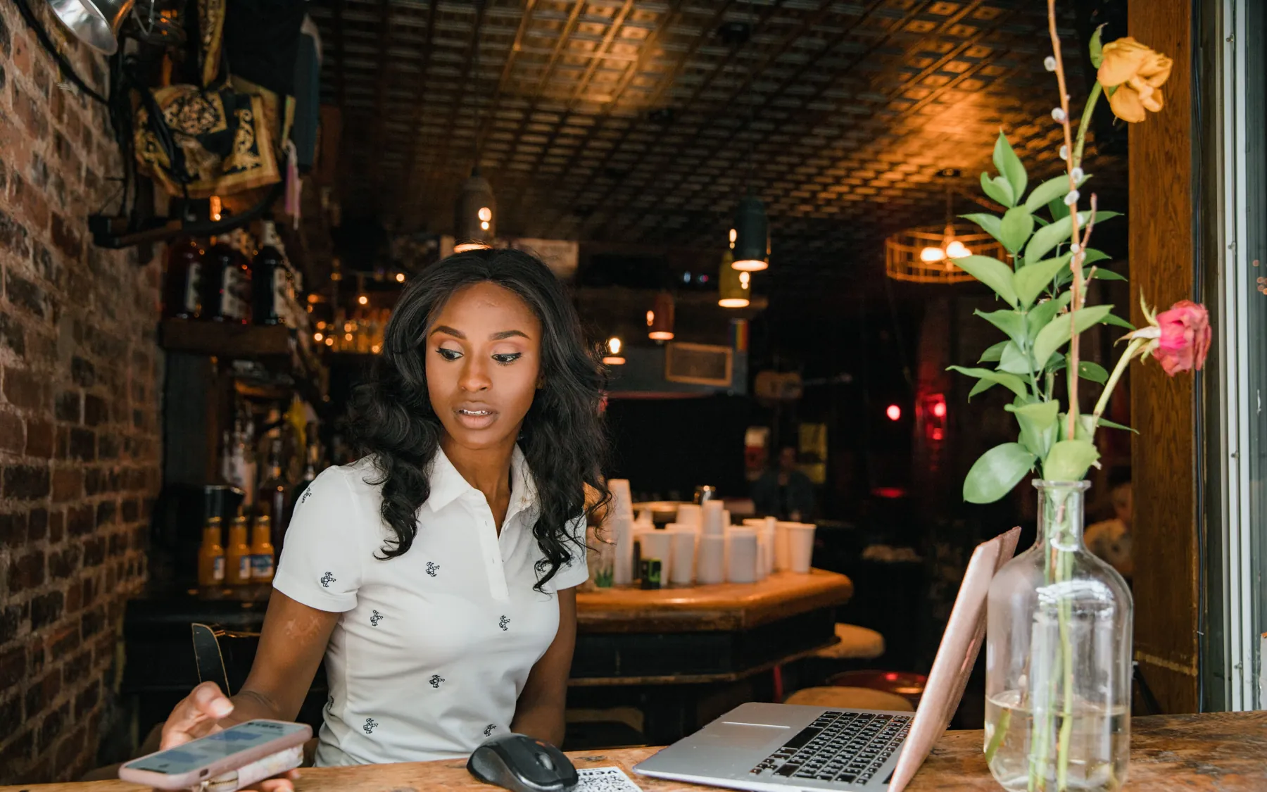 A cafe owner at her counter checking her phone beside an open laptop